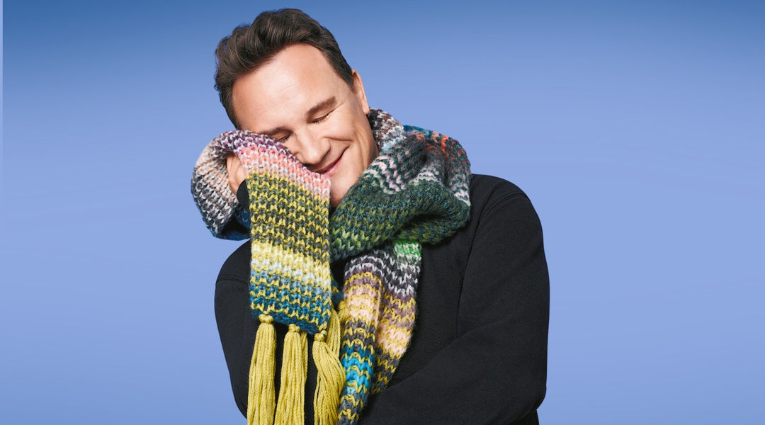 Person smiling while wearing a colorful scarf against a blue background.