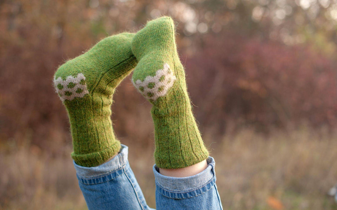 Zwei Füße mit grasgrünen Socken sind vor einer herbstlichen Kulisse in die Luft gestreckt. 